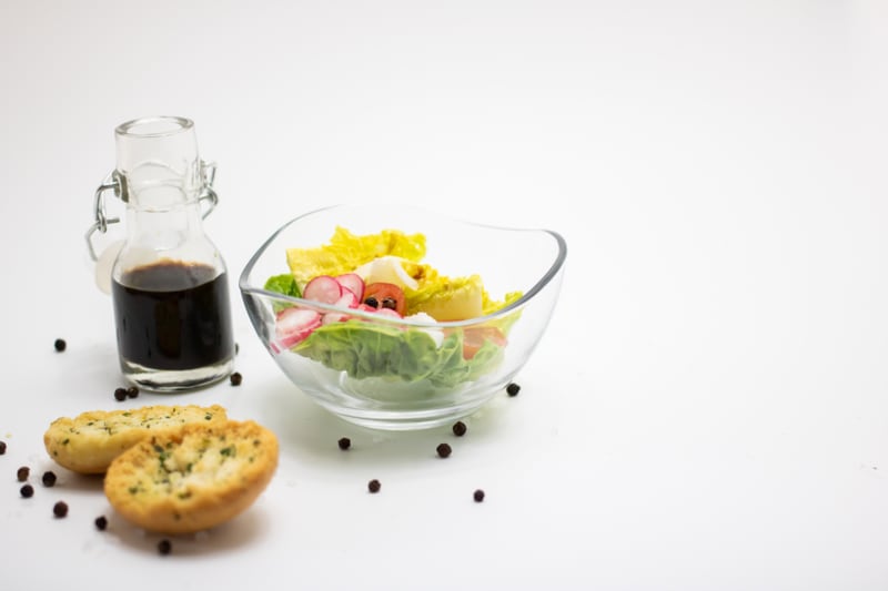 A bowl of salad with bread and a small glass jug of dressing