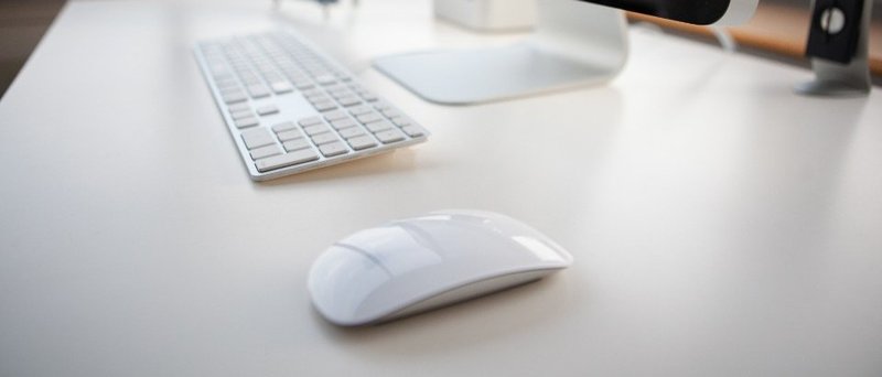 A white computer keyboard and mouse on a desk beneath a monitor stand
