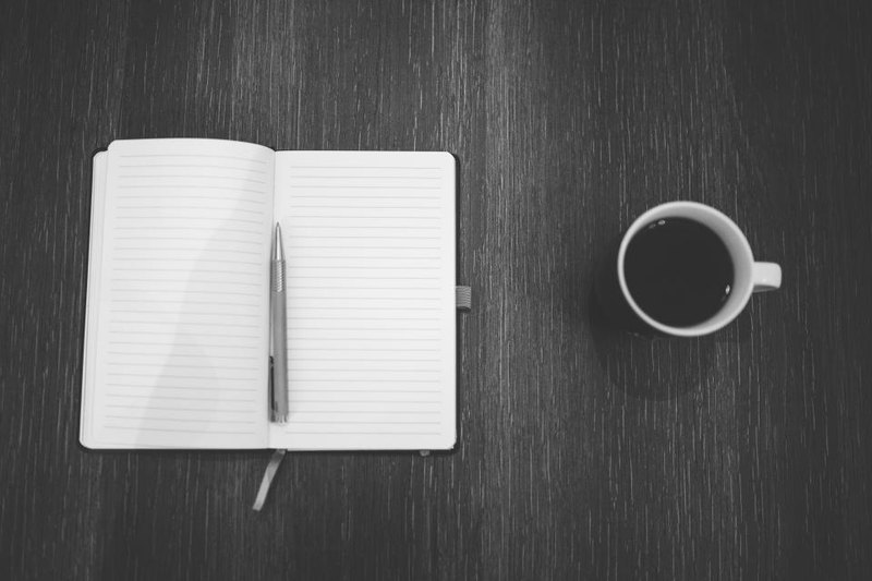An open lined notebook, pen and cup on a dark wooden table