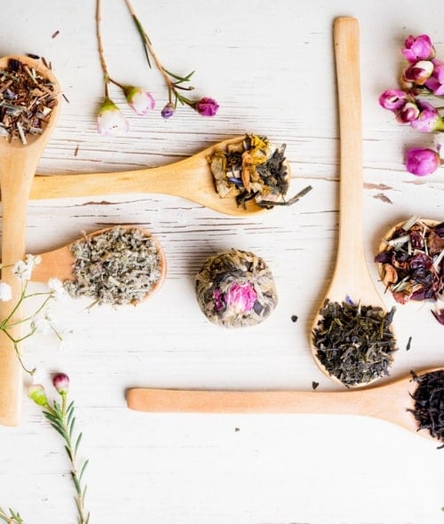 Wooden spoons holding dried herbs and flowers on a pale wooden surface