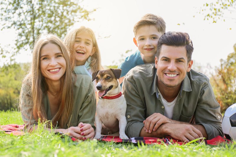Two adults, two children and a dog together on a picnic blanket outdoors