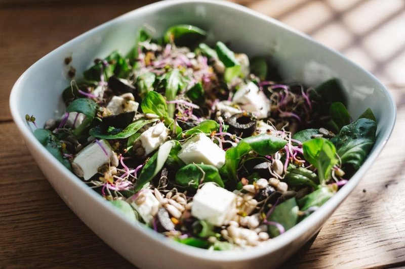 A bowl of leafy salad with sprouts, seeds and white cheese